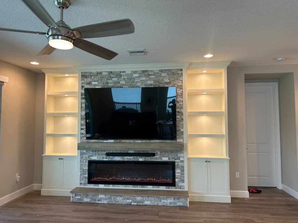 Built-in media wall with lighted shelving and stone fireplace surround