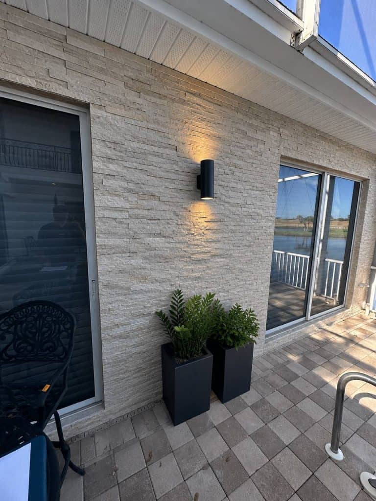 Stacked stone outdoor accent wall with sconce lighting by the pool