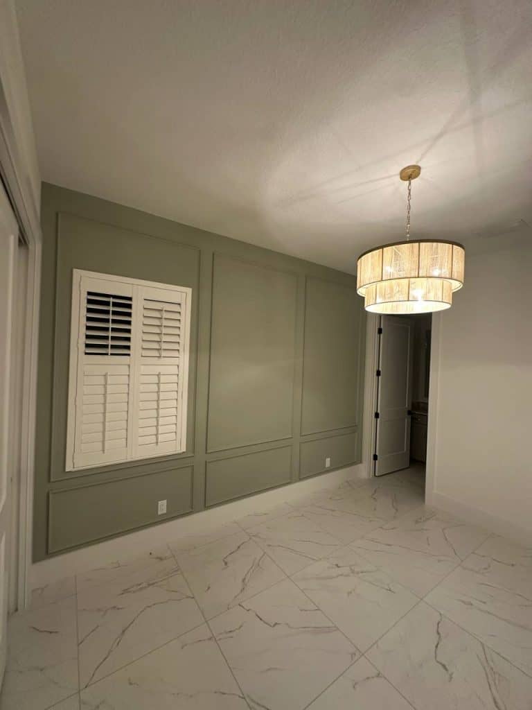 Sage green molding accent wall with plantation shutters